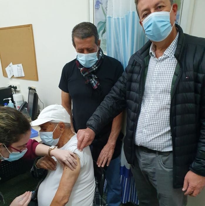ששון בן יעקב מקבל חיסון כשהוא מלווה בראש העיר ישראל גל (מימין) ובבנו אברהם (במרכז). צילום: עיריית קריית אונו