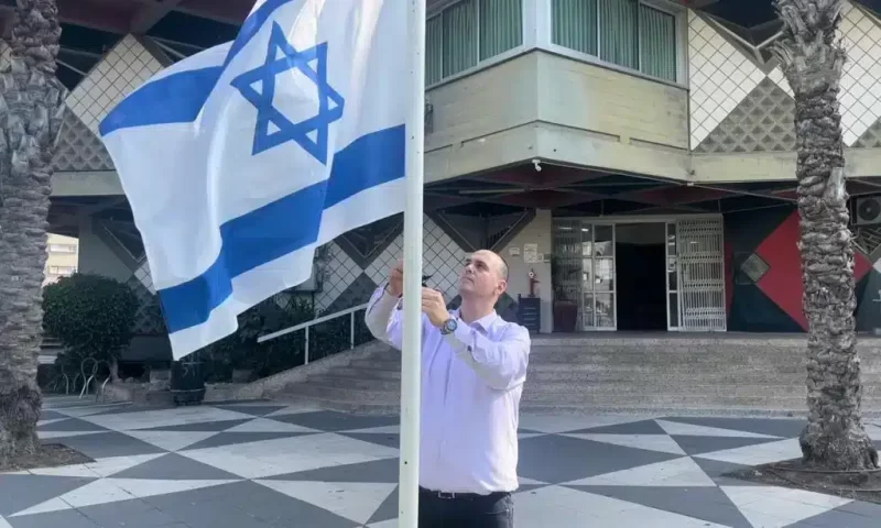 ראש עיריית בת ים צביקה ברוט, עם דגל ישראל על רקע בניין העירייה. צילום: דוברות עיריית בת ים